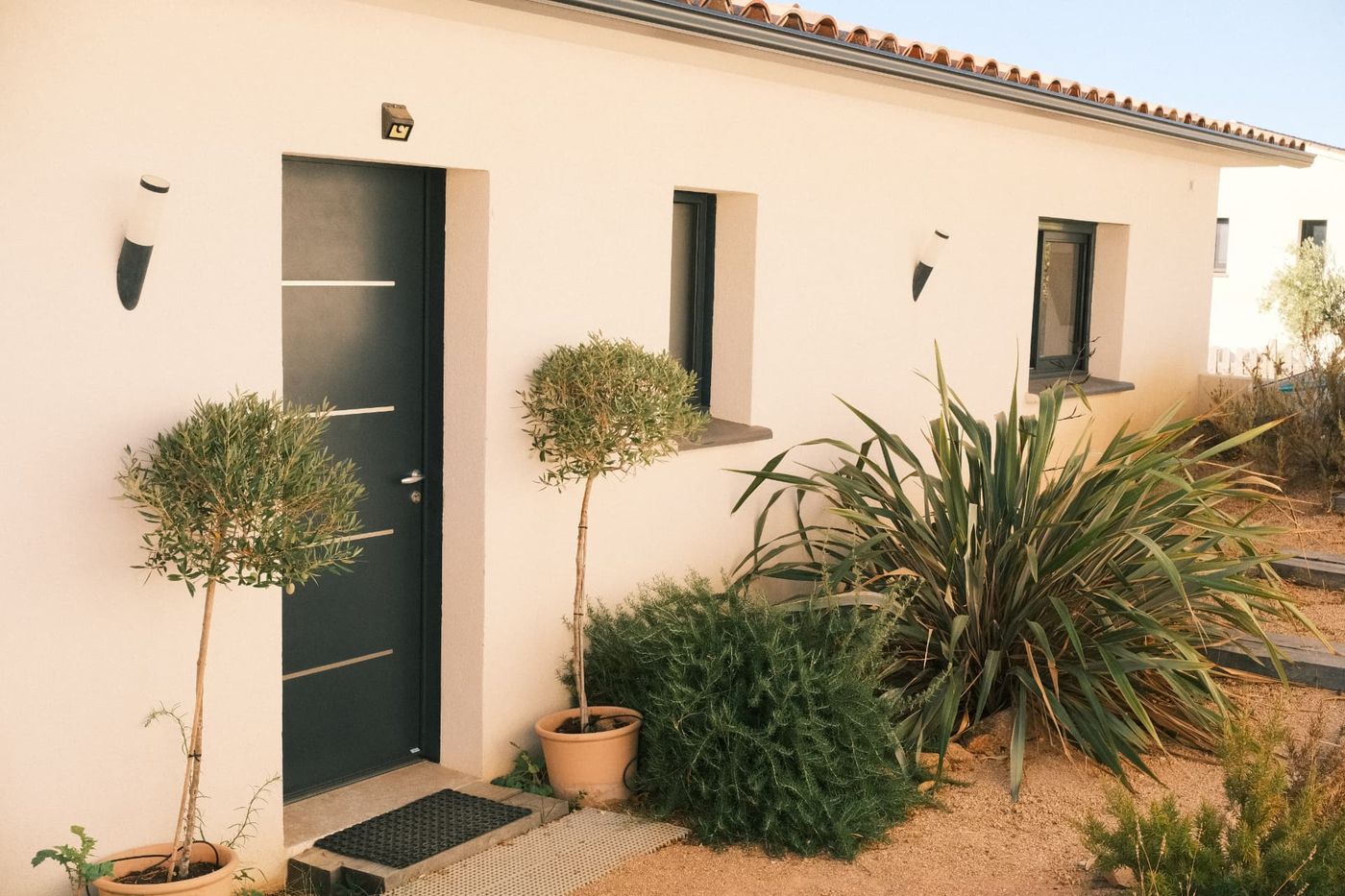 Entrée de la villa avec oliviers en pot et façade claire